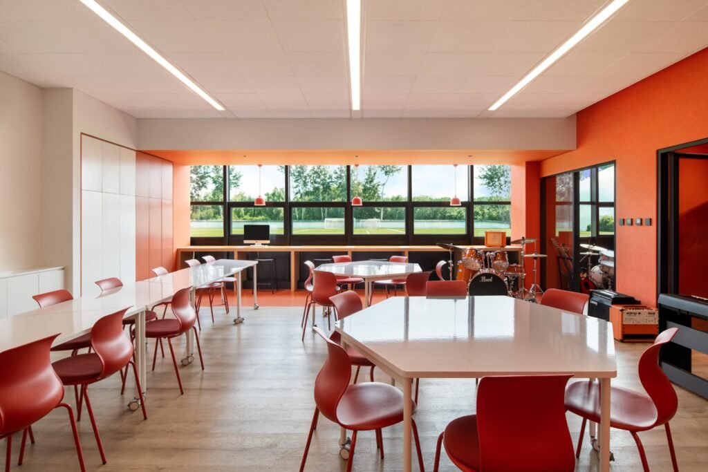 An orange-themed music classroom with hexagonal tables and instruments, balancing neutral teaching areas with vibrant color accents.
