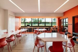 An orange-themed music classroom with hexagonal tables and instruments, balancing neutral teaching areas with vibrant color accents.