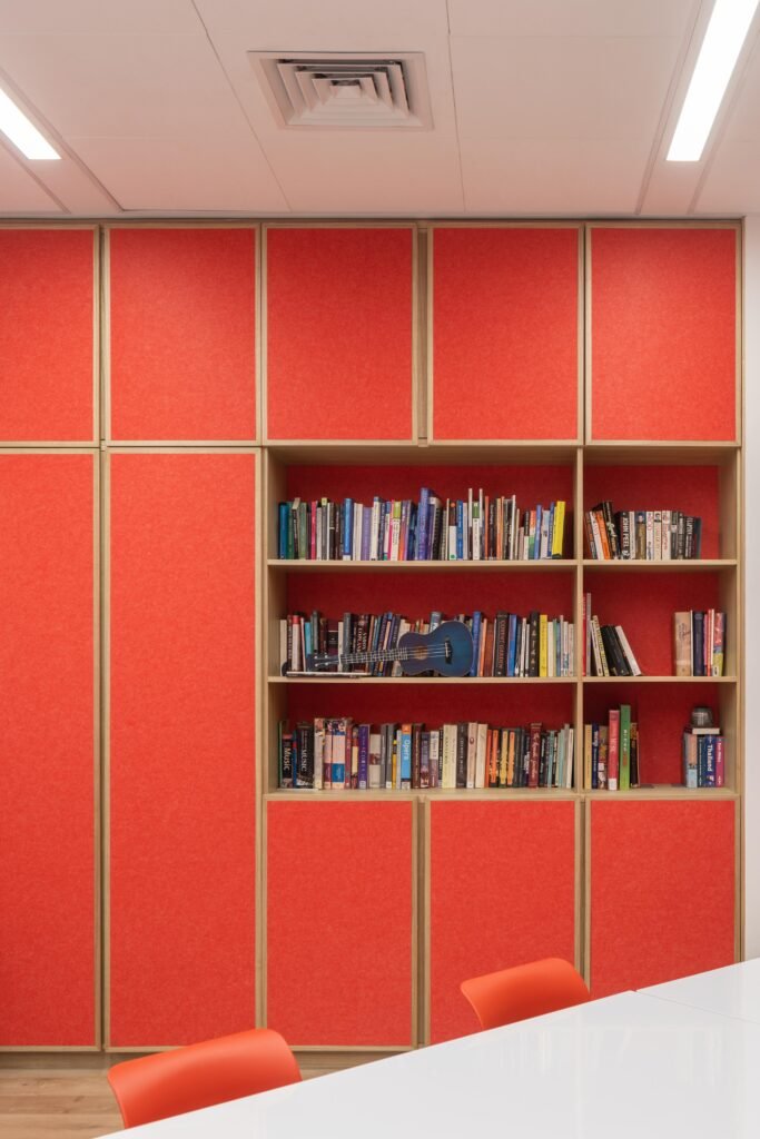 Red felt-paneled built-in shelving unit designed for instrument storage and acoustic management within a music classroom.
