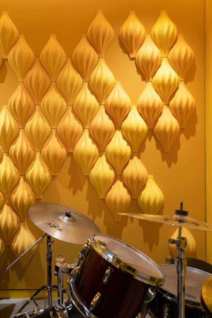 Yellow-saturated practice room for percussion, featuring specialized 3D rhythmic wall tiles to manage acoustics.