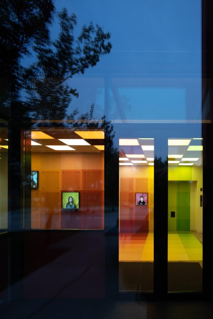 A night view through the glass revealing the saturated red, orange, and yellow grid panels that define the entrance to the music department.