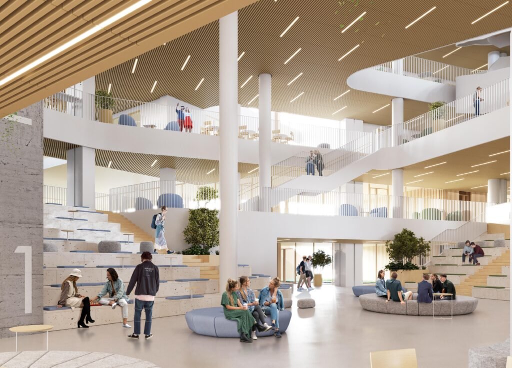 Interior rendering of the primary school’s high-ceilinged central atrium. Strong concrete columns support mezzanine walkways, and the ceiling is lined with warm wood slats. On the left, a large concrete structure features tiered wooden steps where students sit and socialise. Circular grey seating pods are scattered across the floor.