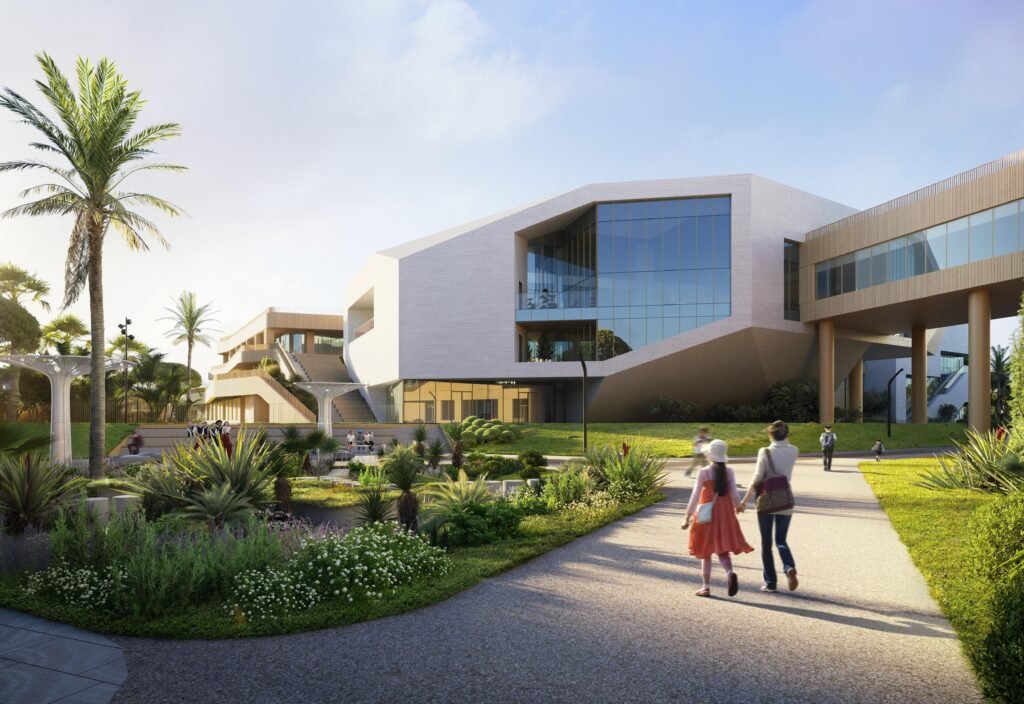 Exterior perspective rendering of the school complex approach. To the left is the public-facing congress centre wing featuring dramatic angular glazing. To the right, an enclosed bridge spans over a wide asphalt footpath. Landscaped lawns with shrubs, ornamental grass, and palm trees frame the walk.