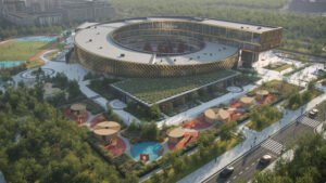 High-angle aerial architectural render of the modern spiral-shaped school complex in Nur-Sultan. The building features an ascending circular structure clad in gold patterned facade, surrounding a central green courtyard with red and green landscaped paths, playgrounds, and adjacent sports fields.