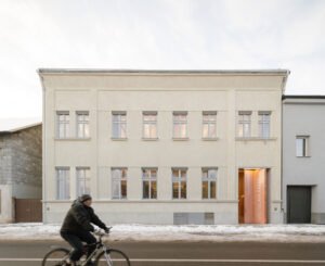 Exterior street-side view of the historic Břetislav Kafka Library in winter, showing its clean beige plastered facade with grey window frames and a cyclist passing by on Sokolská street.
