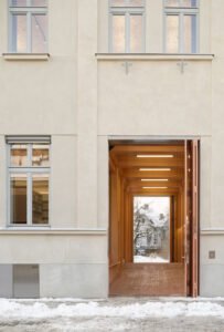 Close-up of the large-format storefront window integrated into the wood-lined passage, offering a direct view of the brightly lit library interior and bookshelves.
