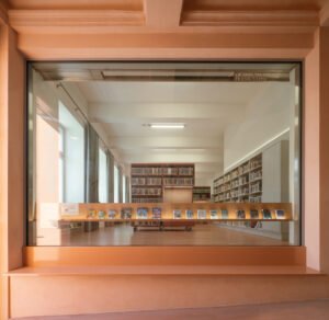 Wide photo of the children's reading room under a wavy white fabric canopy custom-printed with drawings, showcasing pink upholstered mobile benches and small children reading books.