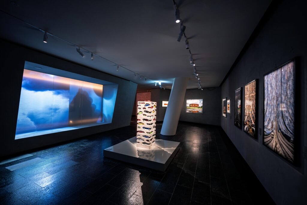 White gallery showing a tall column of stacked plaster blocks encasing small, colourful toy cars.