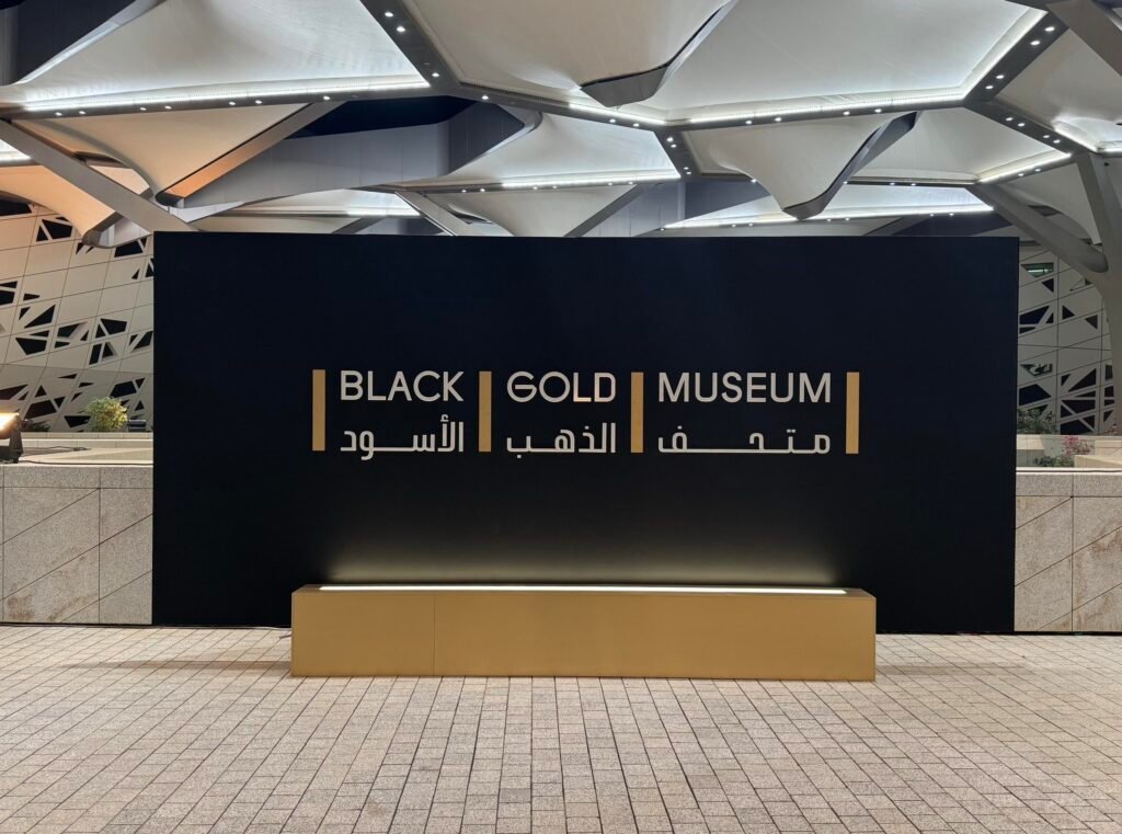 Sleek black sign displaying "BLACK | GOLD | MUSEUM" in English and Arabic on a golden rectangular base outside.