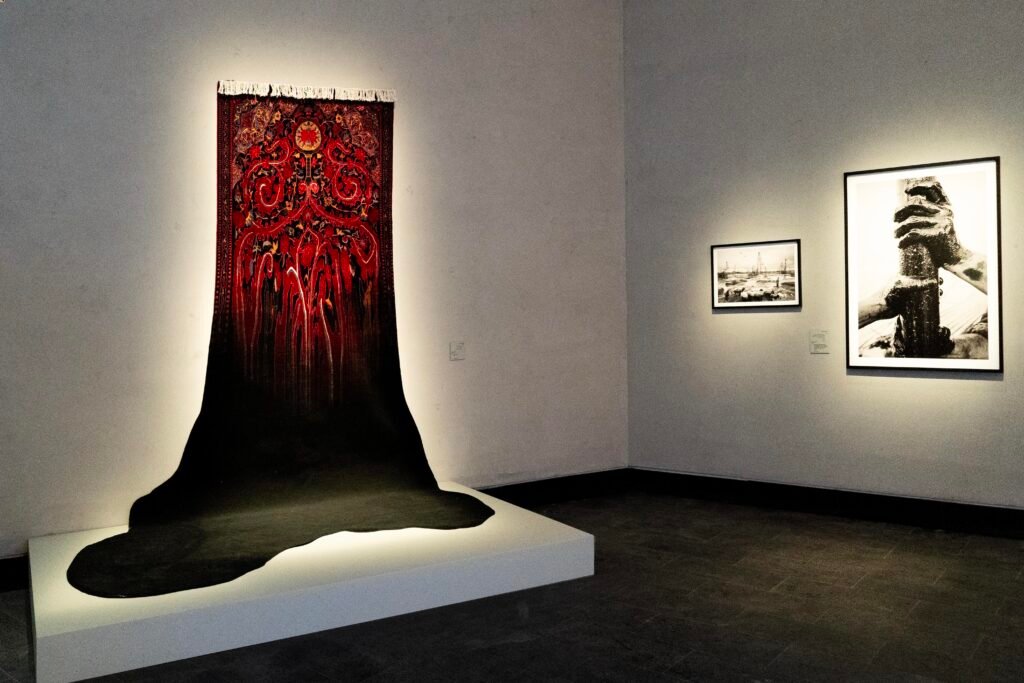 Red Persian carpet on a white wall with a painted black oil spill dripping onto a platform below.