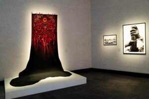 Red Persian carpet on a white wall with a painted black oil spill dripping onto a platform below.