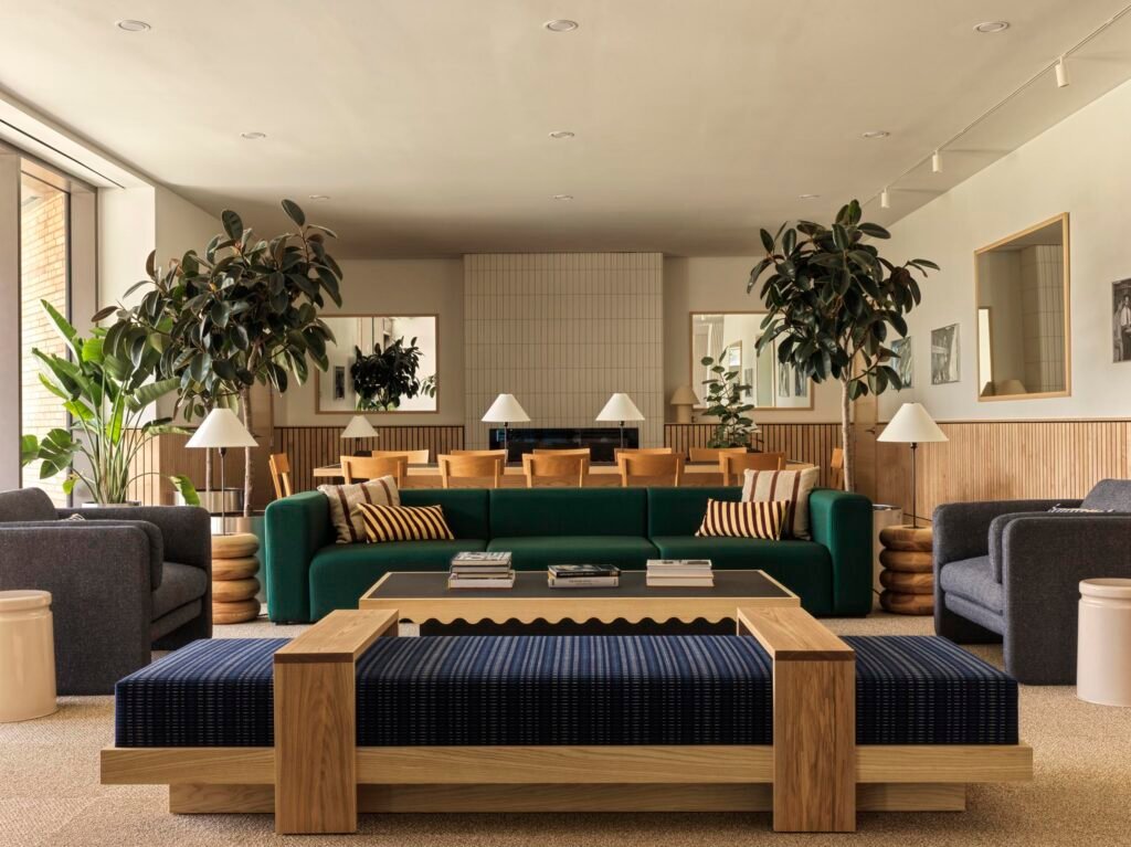 Detail of the Head House lounge with a deep green modular sofa, a blue-and-white patterned bench with a light-wood base, custom round wooden side tables, and grey armchairs arranged around a black coffee table.