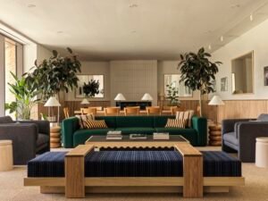 Detail of the Head House lounge with a deep green modular sofa, a blue-and-white patterned bench with a light-wood base, custom round wooden side tables, and grey armchairs arranged around a black coffee table.
