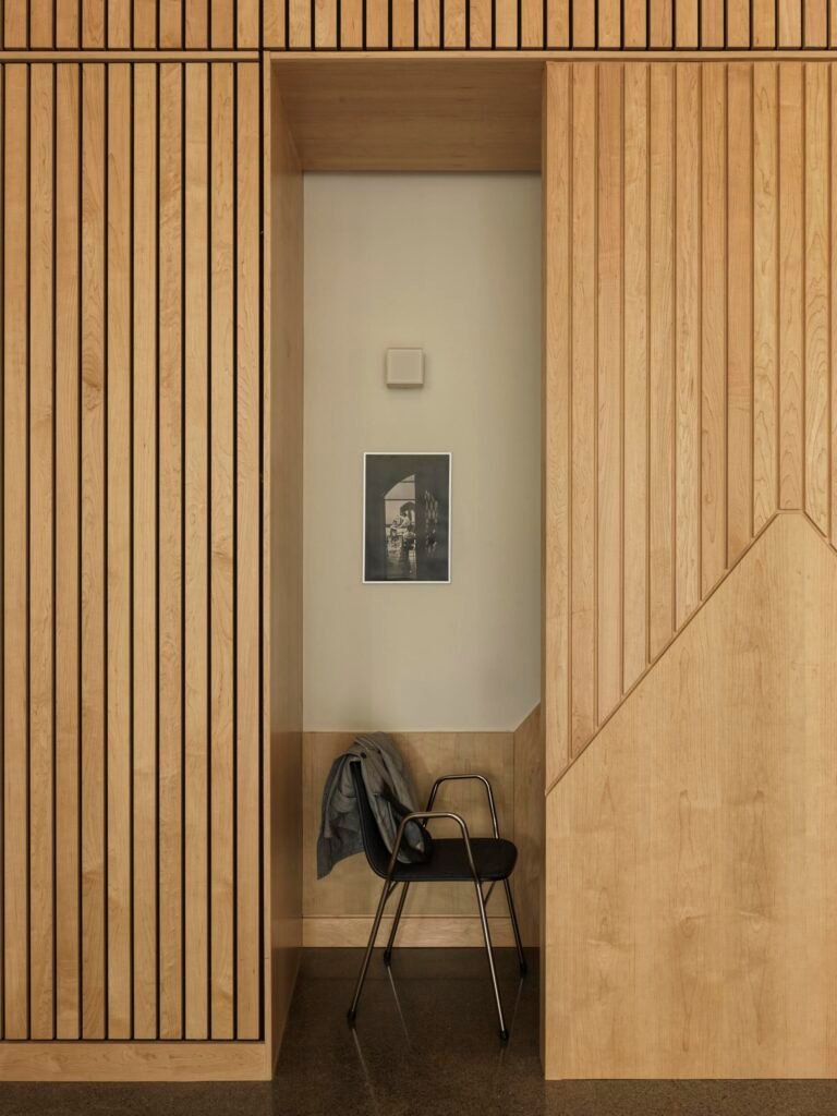  A single student study niche built with vertical slatted light wood panels, featuring a minimalist black chair and a framed black-and-white archival photograph on the inner wall.