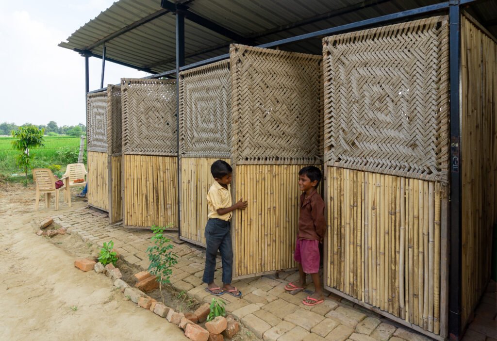Exterior view of the rebuilt school showing lower bamboo reed walls and upper hinged charpai woven panels swung open to allow ventilation and daylight into the structure.
