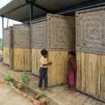 Exterior view of the rebuilt school showing lower bamboo reed walls and upper hinged charpai woven panels swung open to allow ventilation and daylight into the structure.