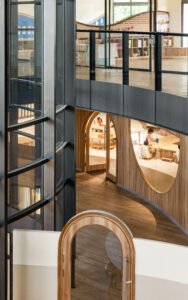 Interior architectural perspective looking down a curved hallway in Vedanya School showing arched doorways, internal glass walls, and peekaboo windows into classrooms.