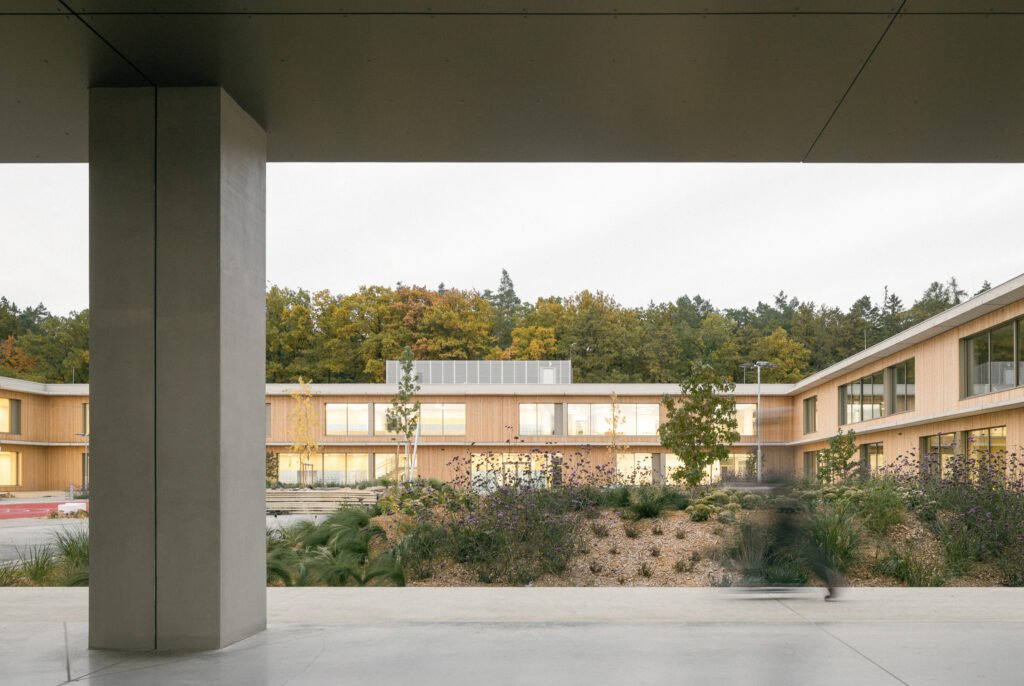 Exterior perspective looking through a covered concrete entrance frame into the central green play courtyard.