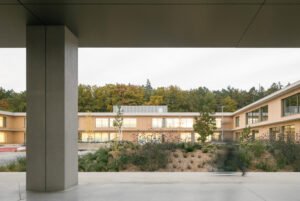 Exterior perspective looking through a covered concrete entrance frame into the central green play courtyard.