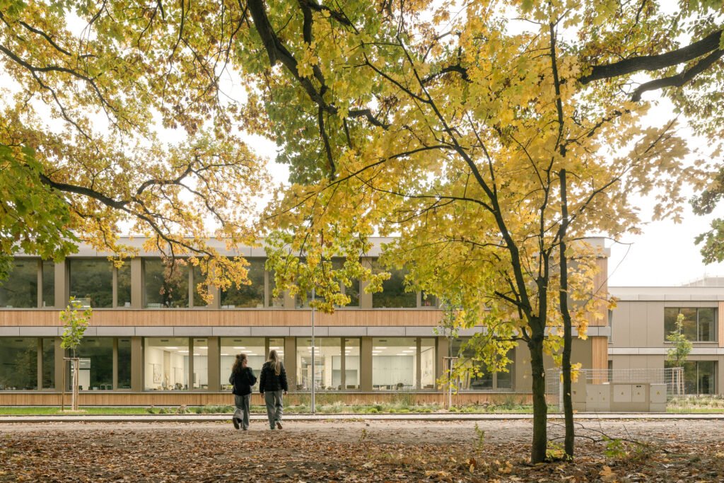 Exterior photograph showing the weathered larch wood facade situated directly along a natural woodland path and tree line.
