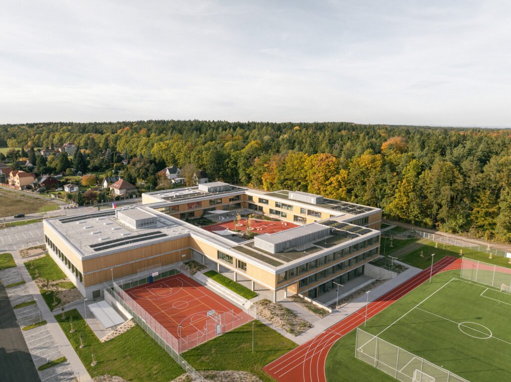 High-altitude aerial photograph displaying the school situated in the countryside between four surrounding Czech villages and forest edge.

