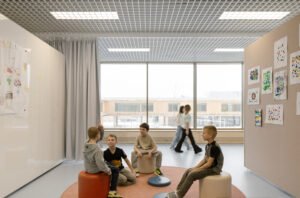 Open-plan educational space furnished with mobile whiteboard walls, acoustic ceiling grid panels, round rugs, and modular student desks.